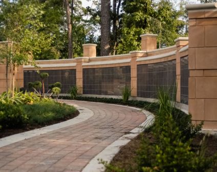 Curved brick paver walkway bordered by planting beds and a stone wall